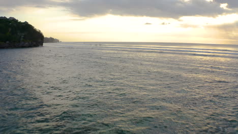 Low-flyover-Indian-Ocean-with-beautiful-small-waves-and-stunning-sunset-with-red-orange-clouds-and-sunshine-in-distance