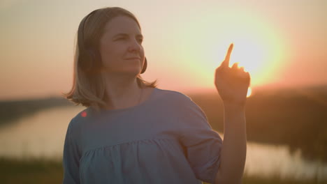 a woman wearing a headset smiles contentedly while gently moving her body as if dancing. she is bathed in the warm, golden light of the setting sun, creating a peaceful and joyful atmosphere