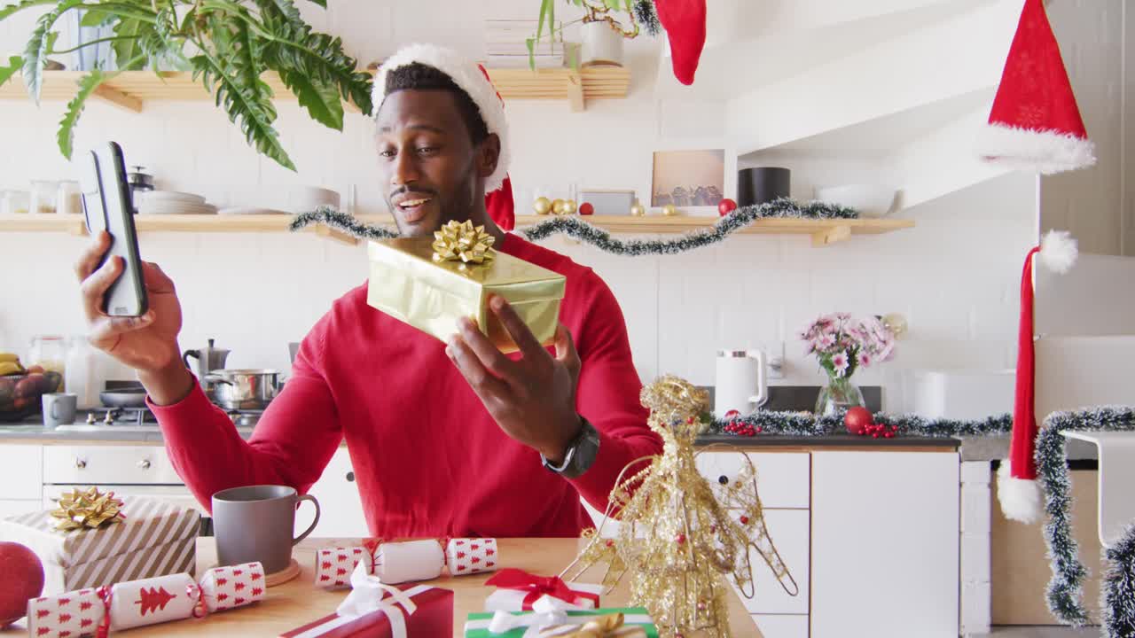 hombre afroamericano feliz con sombrero de papá noel, usando teléfono inteligente para llamadas de video.