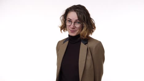 Portrait-closeup-of-adorable-european-woman-wearing-brown-jaket-and-stylish-glasses,-curly-short-hairstyle-posing-on-camera-with-lovely-smile-and-wink-once,-isolated-over-white-background