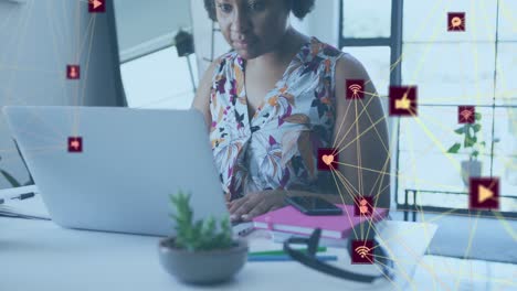 Animation-of-globes-of-digital-icons-over-african-american-woman-using-laptop-at-office