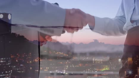 Mid-section-of-businessman-and-businesswoman-shaking-hands-and-exchanging-cards-over-cityscape