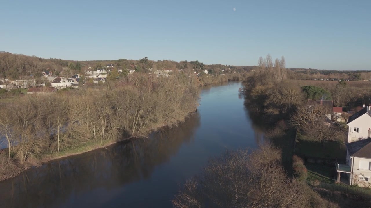 Una veduta aerea segue una dolce ansa del fiume oltre un piccolo villaggio e la campagna aperta nella Valle della Loira, Francia
