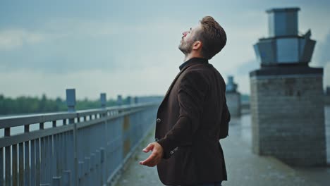 man looking up at cloudy sky by the river