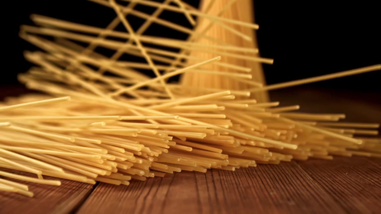 Spaghetti crudi che cadono e si spargono su un tavolo di legno al rallentatore