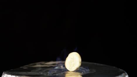 bitcoin spinning on silver surface in blue flame burning against black background, positioned on bottom of frame.