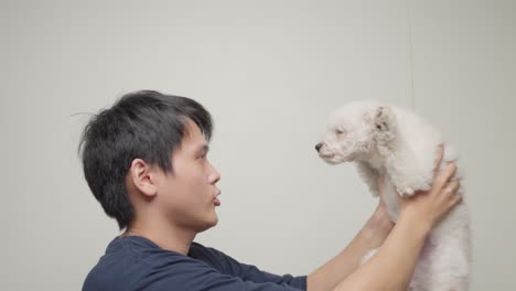 asian man holding white poodle puppy on his outstretched arms, looking each other frontal, side view