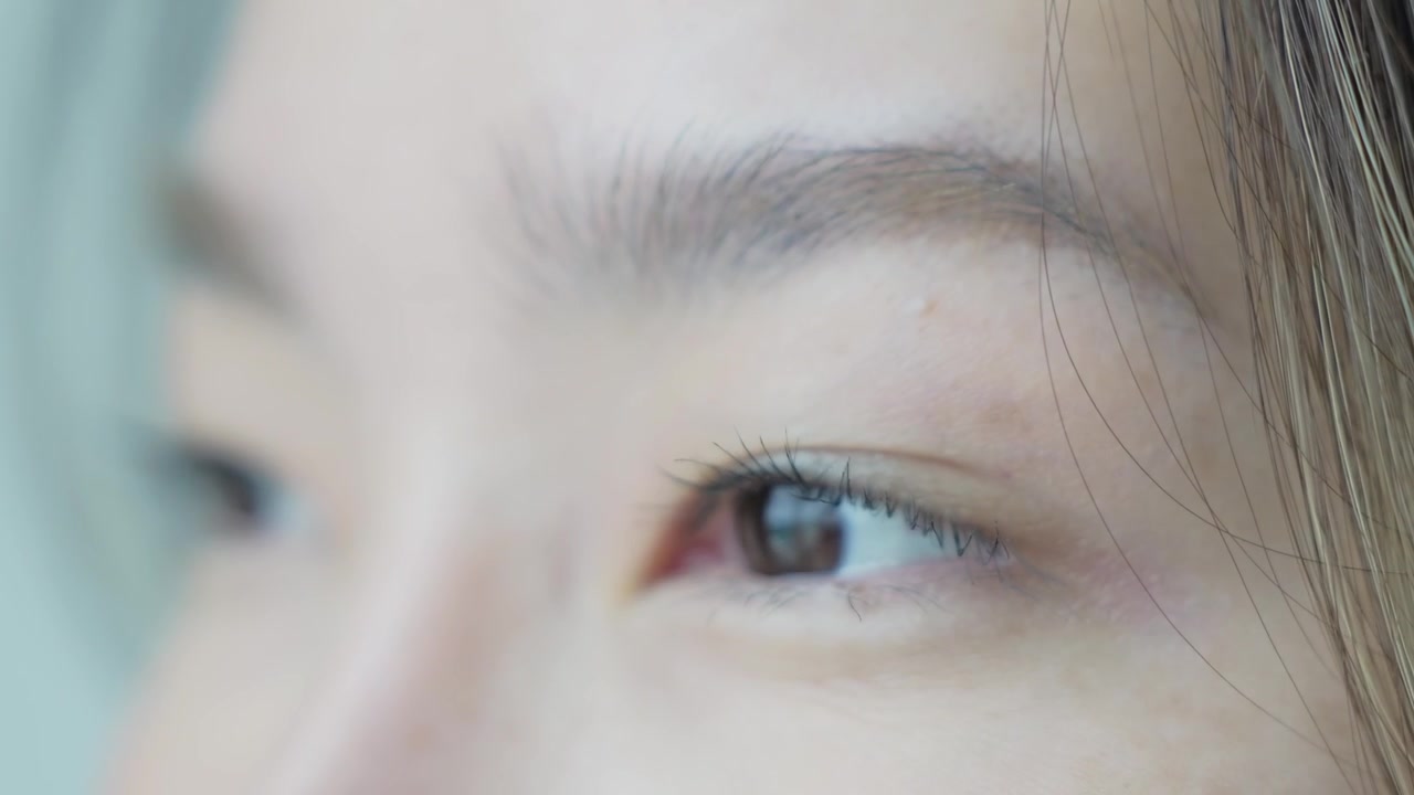 柔らかな自然光の中で、ナチュラルメイクのアジア人女性の目のクローズアップ。詳細な虹彩、まつげ、表情を捉えている。