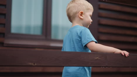 little boy walks touching brown wooden beam on terrace