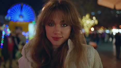 una mujer sonriente en un parque de atracciones disfrutando de luces festivas en primer plano.