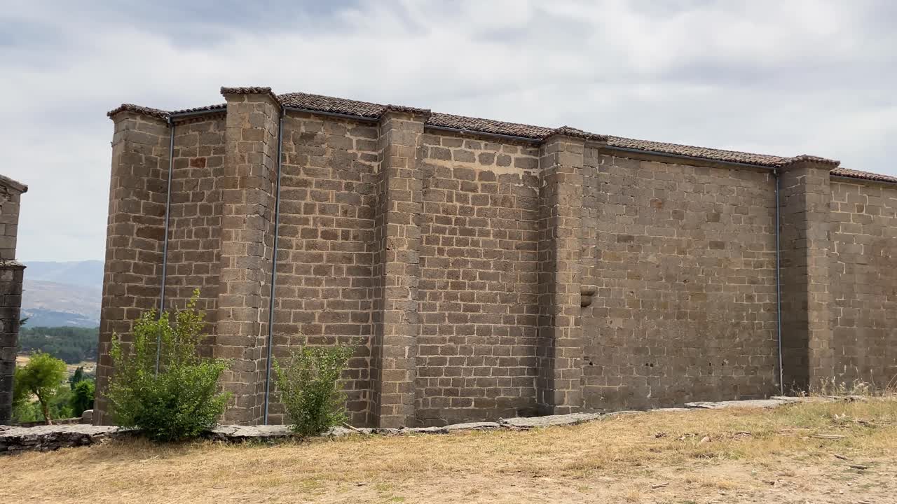 lateral recording of the impressive stone structure of a sanctuary from the back, appreciating its buttresses and ashlars, next to it is its bell tower and in the background we see a town