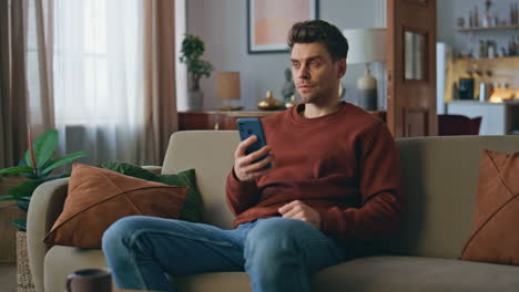 pensive freelancer reading email on smartphone at couch. man looking cellphone