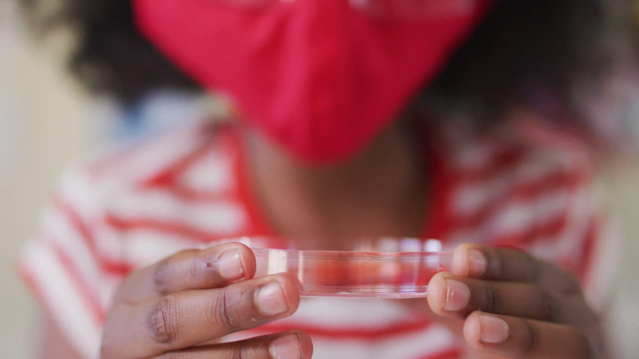 niña con máscara facial y gafas protectoras sosteniendo un contenedor con productos químicos en el laboratorio