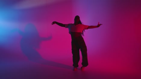 full length studio shot of young woman dancing against blue and pink lit background 2