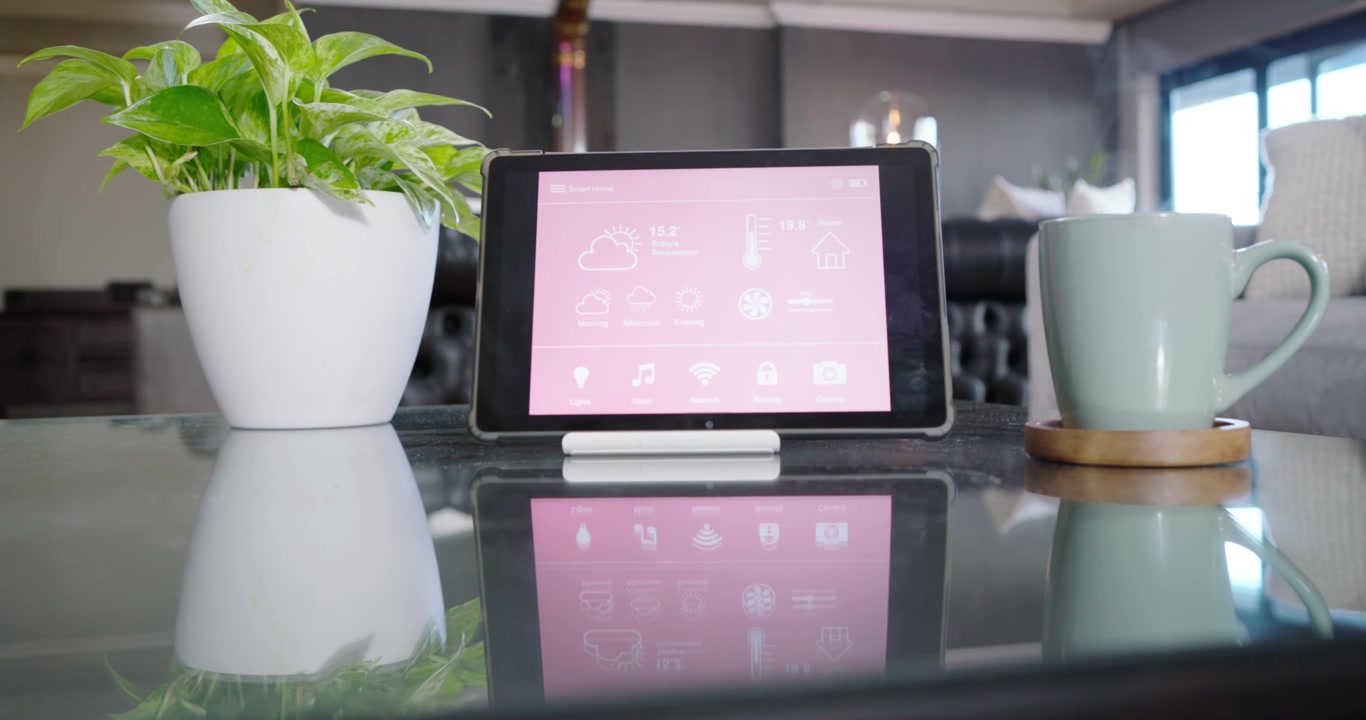 Camera is moving, focusing on tablet on glass table with plant and mug, showing pink reflection