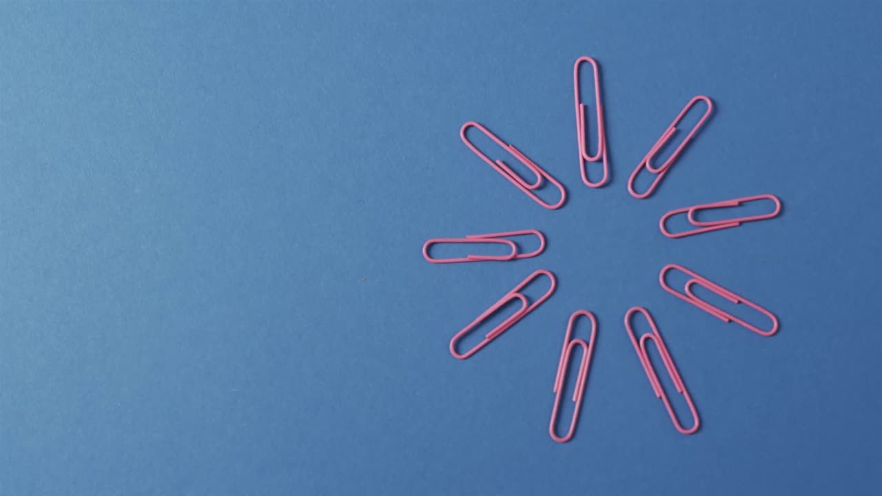 Overhead view of pink paper clips arranged with copy space on blue background, in slow motion