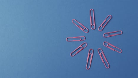 overhead view of pink paper clips arranged with copy space on blue background, in slow motion