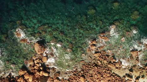 Zoom-Aéreo-En-Vista-Del-Mar-Turquesa-Claro-Y-Las-Olas-Aplastando-Rocas-De-Color-Rojo-En-La-Playa-Cerca-De-La-Playa-De-Rampa-En-La-Isla-De-Gozo,-Malta