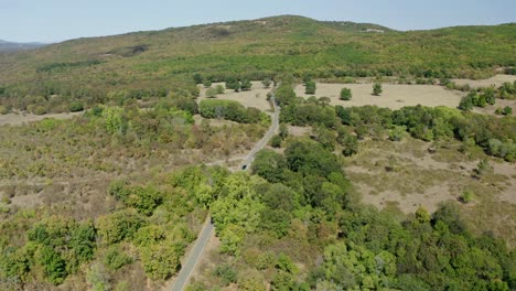 Toma-Aérea-De-Seguimiento-De-Un-Automóvil-En-La-Carretera-En-Las-Montañas-Ródope-Durante-El-Día-Soleado.