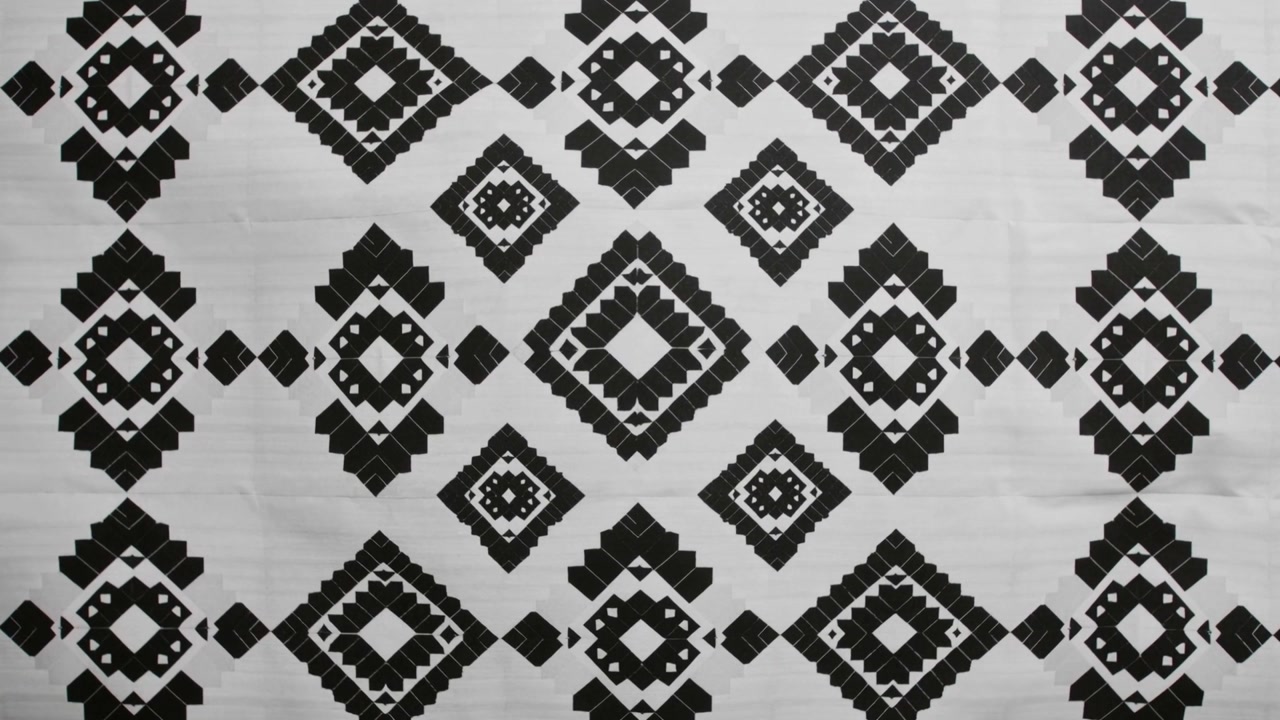 Shifting camera showing repeating nested diamond motifs sliding on white panel, with faint creases