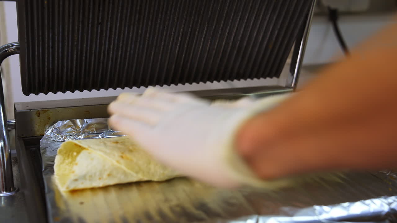 Hands of cheef put shawarma on grill. Preparing street food in cafe. Tasty pita with vegatables and cheese.