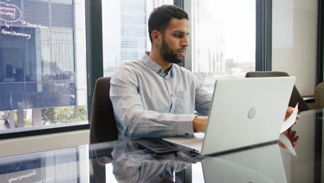 working in office, man using laptop and holding documents at desk