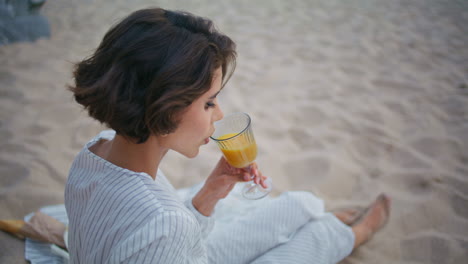 una chica tranquila disfrutando de un picnic en la orilla del mar. una mujer bonita bebiendo jugo de naranja.