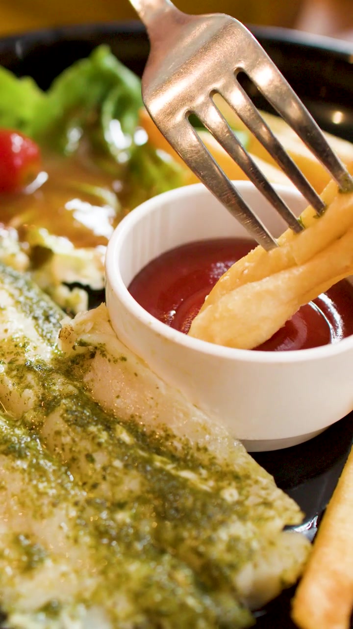 Primo piano di una forchetta che intinge una patatina fritta croccante in una ciotola di ketchup