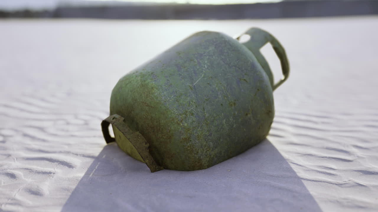 Bombola di gas verde appoggiata su un terreno sabbioso durante le ore del tramonto