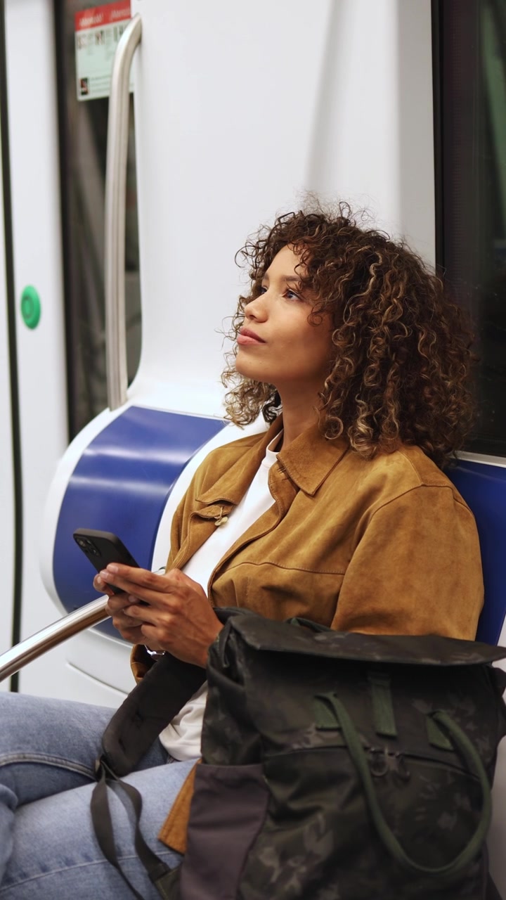 Young Woman Using Smartphone and Looking Up on Subway Train
