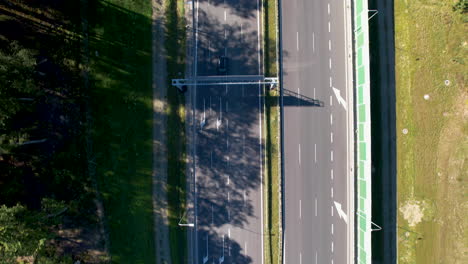 Una-Vista-De-Una-Carretera-Muy-Transitada-Cerca-De-Wielki-Kack,-Gdynia,-Polonia,-Con-Autos-Corriendo-Y-Bosques-Proyectando-Sombras-En-El-Lado-Izquierdo,-Vista-Desde-Una-Perspectiva-Aérea-Bajo-La-Luz-Del-Sol