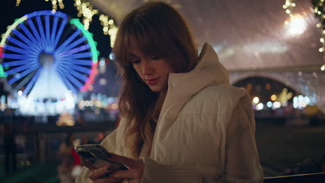 girl texting phone amusement park illuminated with festive lights closeup.