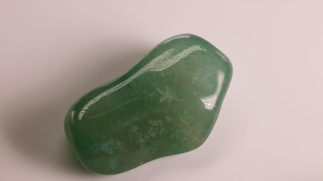 A green aventurine stone spins smoothly on a white surface, highlighting its glossy texture and natural patterns
