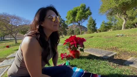 close up of hispanic female sitting on grass at cemetery paying her respects, smiling on a clear sunny day