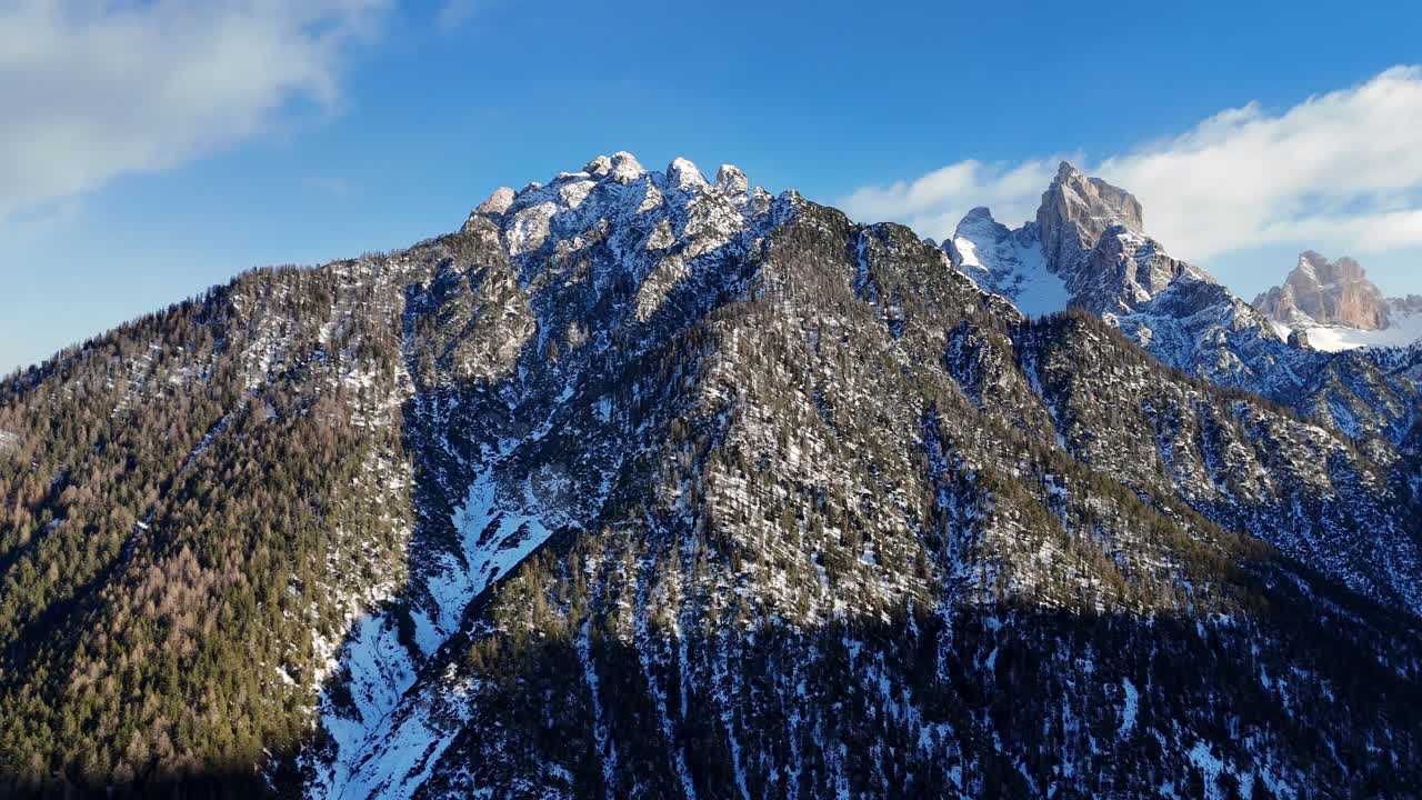 Mountain in the Dolomites covered in snow and trees on a bright day, during winter season (drone footage)