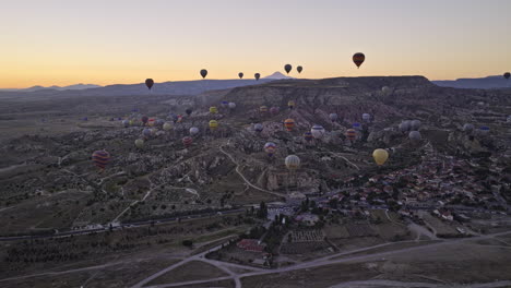 Göreme-Turquía-Antena-V44-Sobrevuelo-Campos-Abiertos-Con-Vistas-Al-Pueblo-De-çavuşin-Y-Mesa-Montaña-Plana-Al-Amanecer-Con-Coloridos-Globos-Aerostáticos-Volando-Alto-En-El-Cielo---Filmado-Con-Cine-Mavic-3---Julio-De-2022