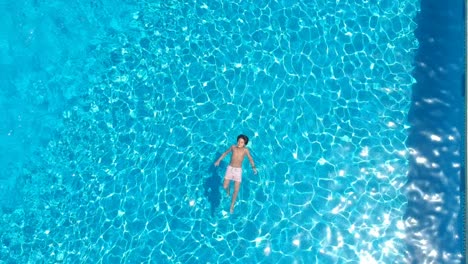 From-a-drone,-a-child-swims-calmly-over-a-pool-of-blue-water