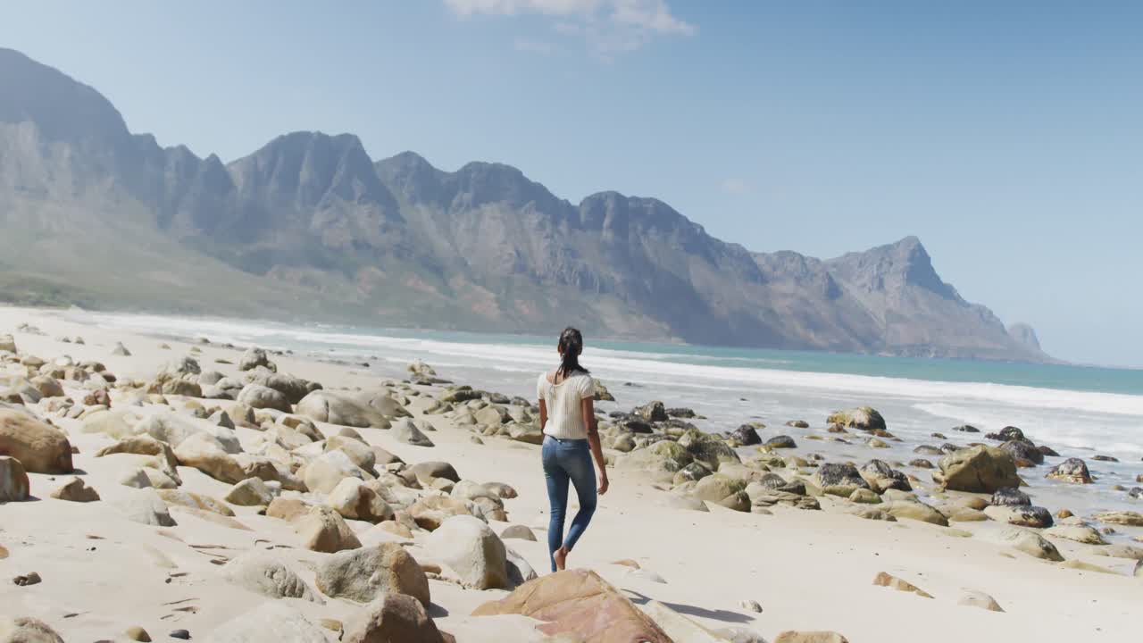 mujer afroamericana caminando por la playa mientras hace senderismo