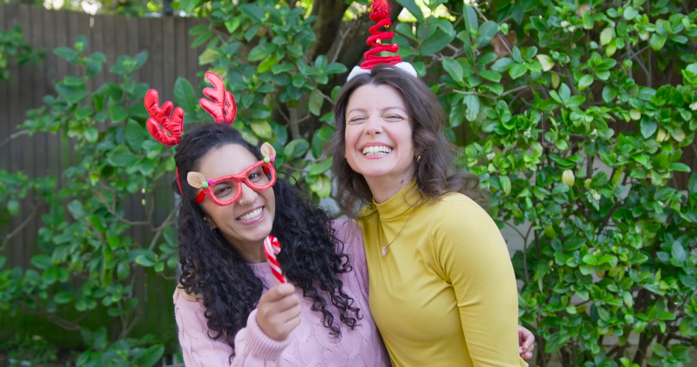 Amigas diversas reaccionando a la aparición de un bastón de caramelo, posando en el patio trasero con gorros de Navidad