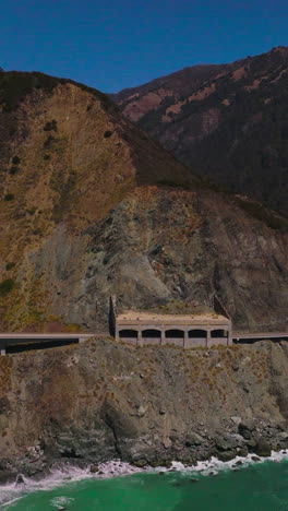 road connecting the mountains at the coastline of california. beautiful sight of the rugged rocks at the backdrop of blue clear sky. vertical video