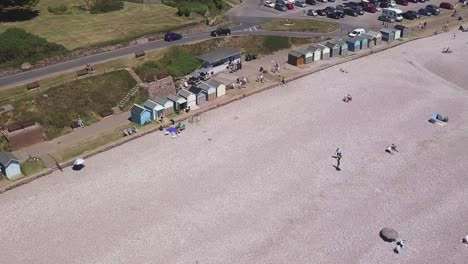 Aerial-High-to-Low-shot-of-tourists-on-a-pebble-beach-by-a-parking-lot,-STATIC-CROP