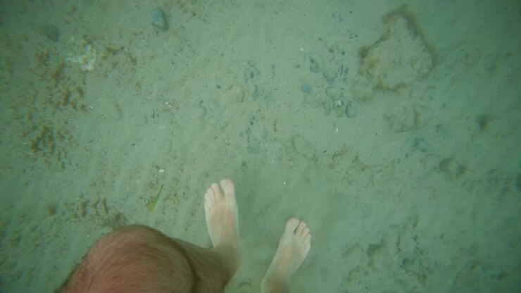 Un piede che poggia sul fondale sabbioso e limpido nell'acqua turchese dell'oceano, godendosi una vacanza rilassante e le ferie estive.