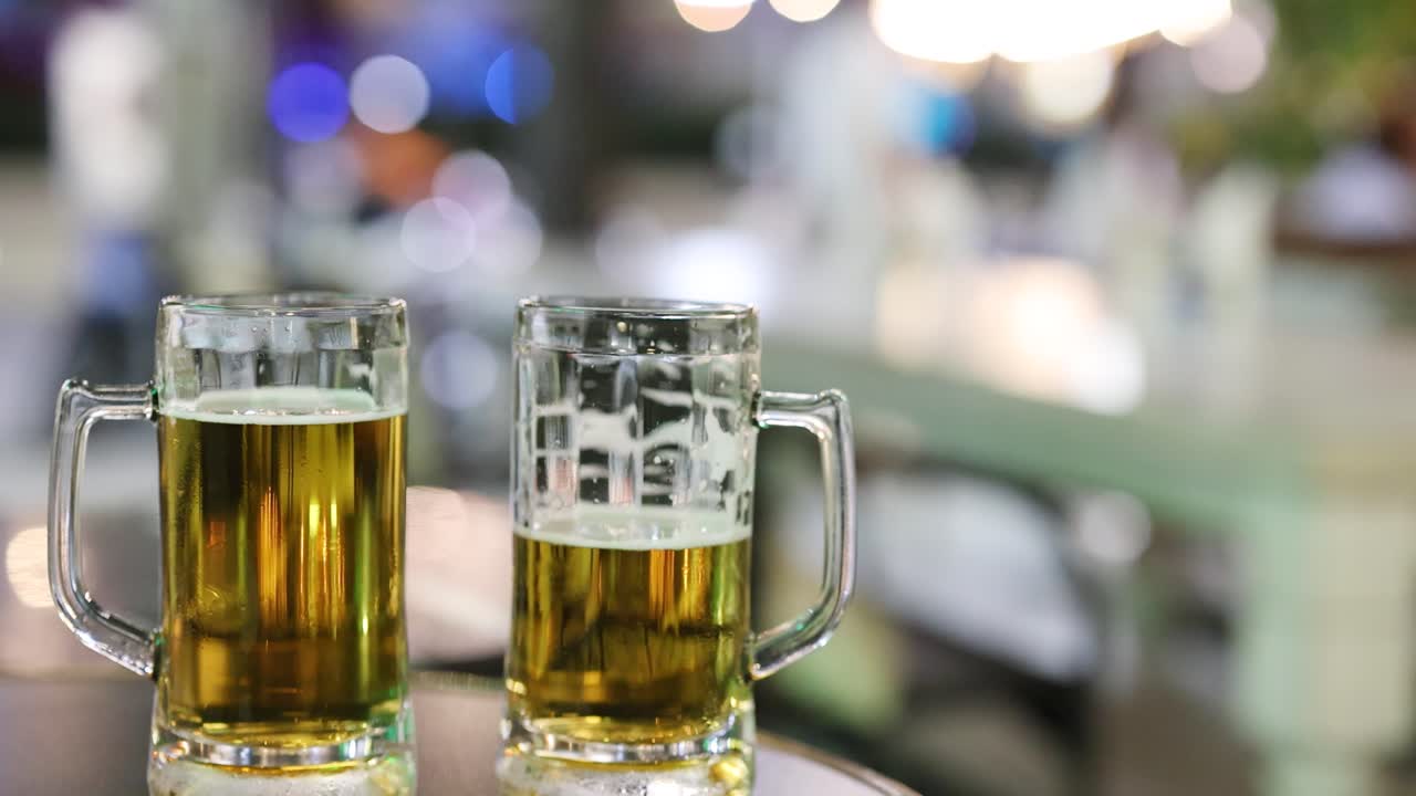 Two beer mugs on a table with blurred night lights in the background, capturing the vibrant nightlife of Phuket