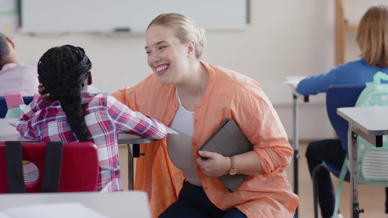 Op school houdt een lerares een tablet vast, glimlacht en praat met een leerling in het klaslokaal.