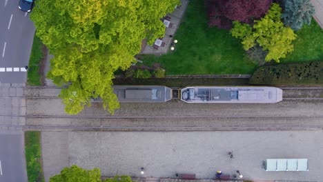 Aerial-Szczecin-City,-Tram-driving-on-rails-through-city-streets-approaching-a-station,-Top-down-view