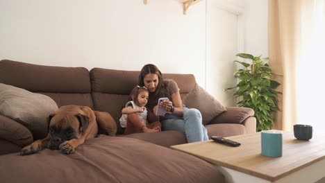 boxer dog relaxing by mother and girl using cellphone on sofa