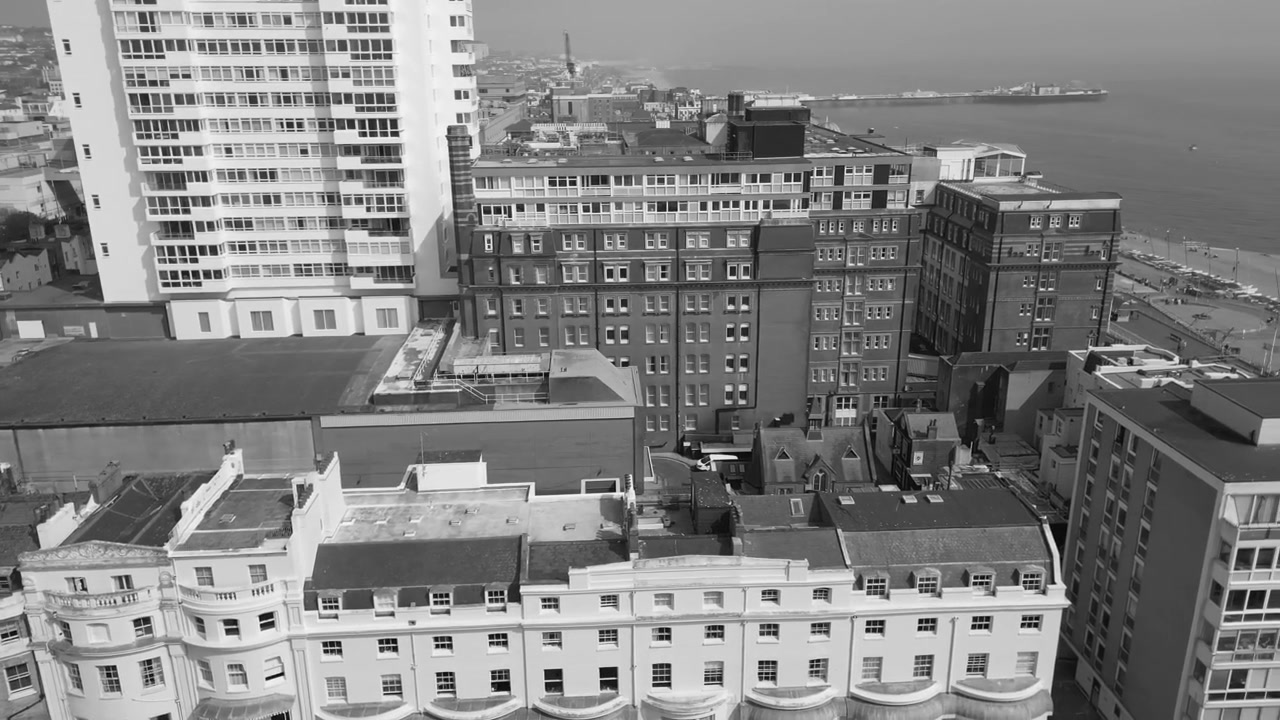 Ripresa aerea in bianco e nero con drone che mostra il lungomare di Brighton con Marine Parade, fitti edifici costieri, strade, passeggiata, spiaggia e il Canale della Manica visibili a Brighton, Inghilterra.
