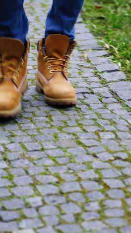 stylish man's legs outdoors. male in brown boots walking a stone path. man's feet wearing jeans and shoes walks on terrace in autumn time. close-up. vertical video