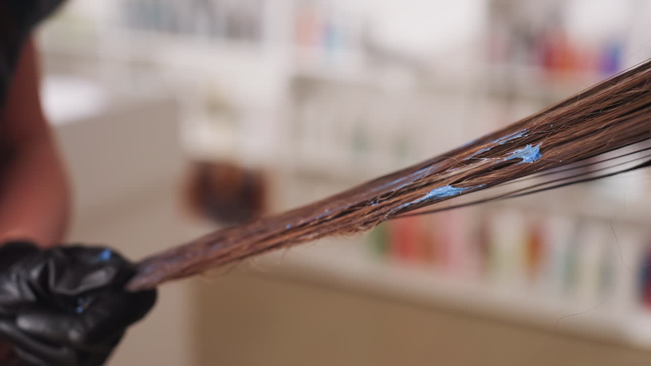 creating clean hair sections for coloring process, professional hairstylist carefully dividing hair for dye application, expert stylist using gloves to section brown hair with meticulous care