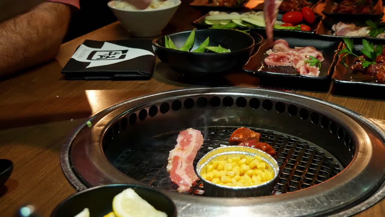 Placing strips of bacon on yakiniku grill embedded into dining table at a Japanese BBQ restaraunt with tongues